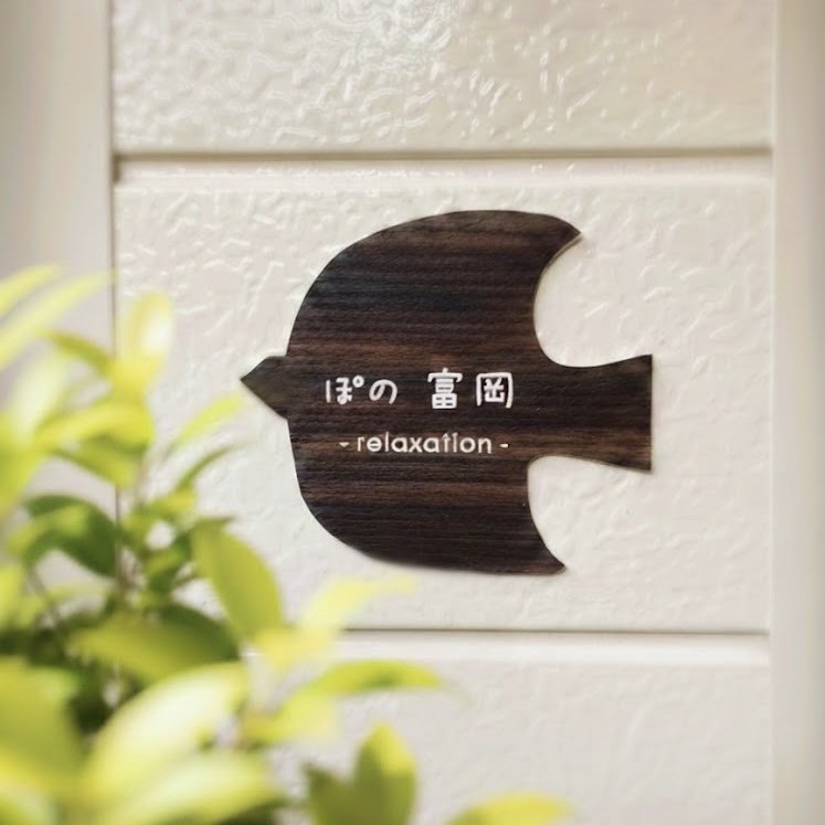 白い壁に掛かった、ぽの富岡の看板